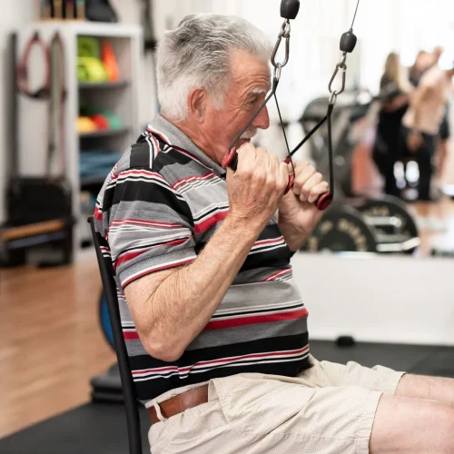 Older gentleman sitting on a chair pulling down weight machine